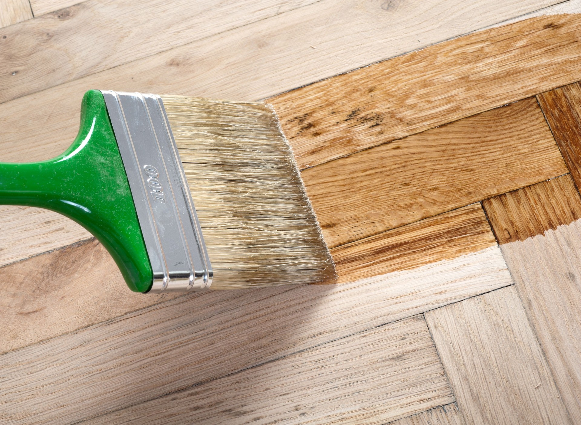A paintbrush applying varnish to a wooden floor